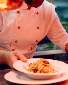 Chef plating pasta in a restaurant kitchen